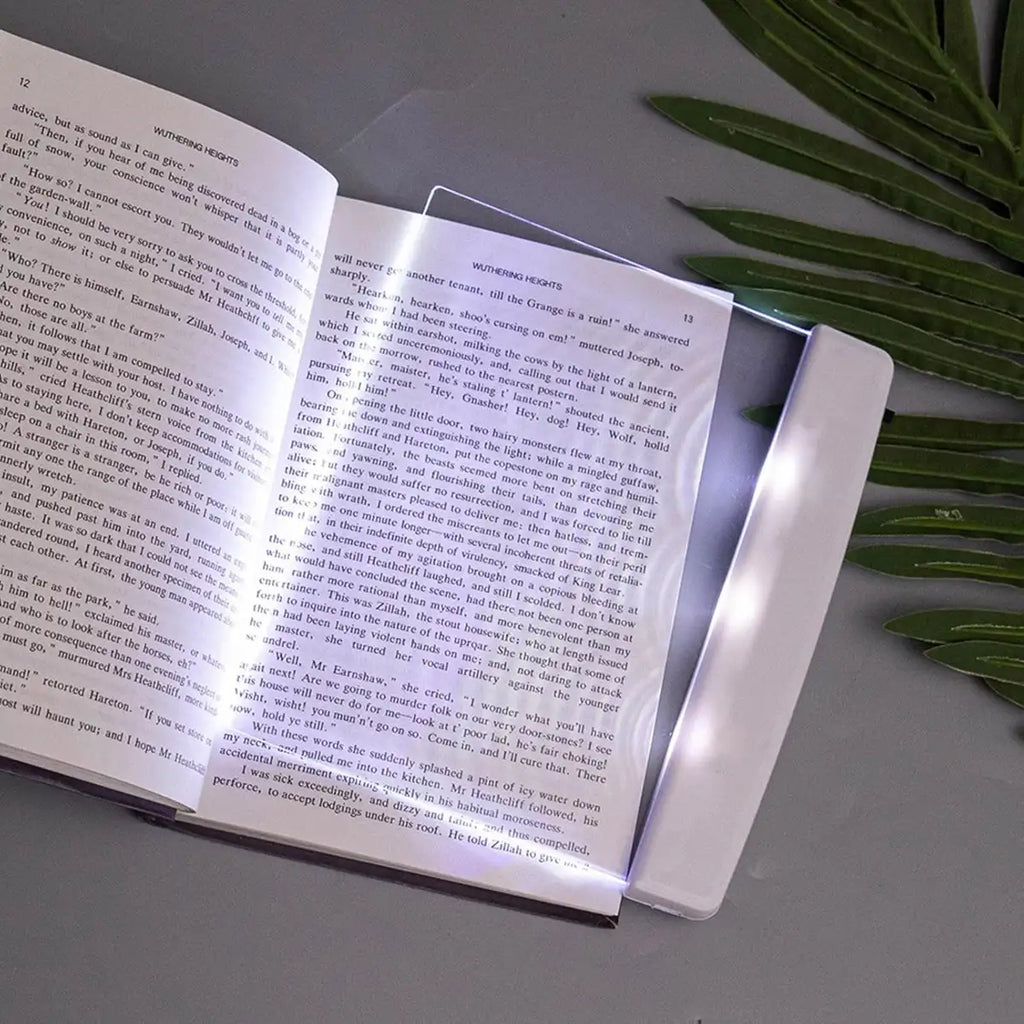 Book with a light on a gray surface next to green leaves