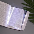 Book with a light on a gray surface next to green leaves