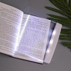 Book with a light on a gray surface next to green leaves
