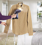 Person using a handheld steamer on a beige shirt in a home setting.