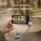 Hand holding a smartphone with a gimbal stabilizer, showing a blurred outdoor scene on the screen.