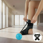 Person using a black ankle support brace with a blue massage ball on a wooden floor.